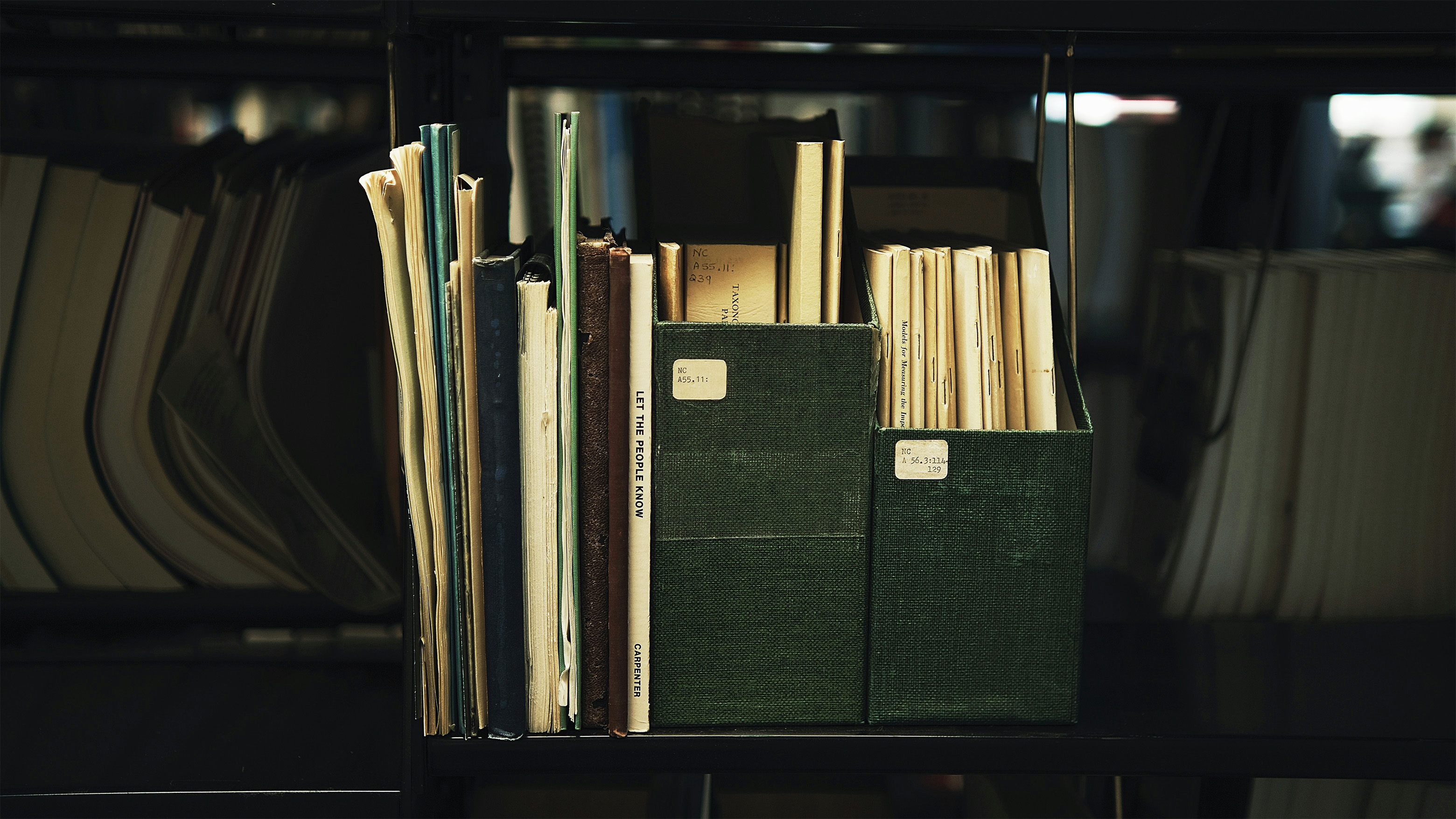 A bookshelf filled with lots of books and papers, some of them divided into shelf organizers. One book spine in the middle reads Let the People Know.