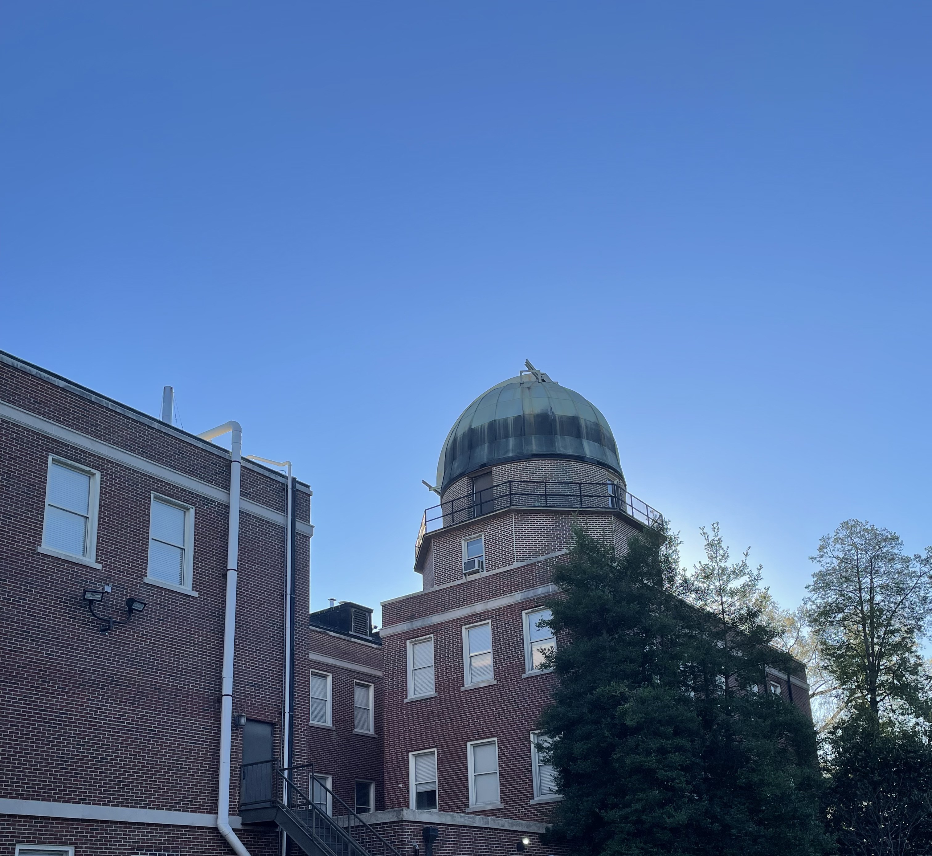 A round observatory on the top of a brick building against a brilliant blue sky.