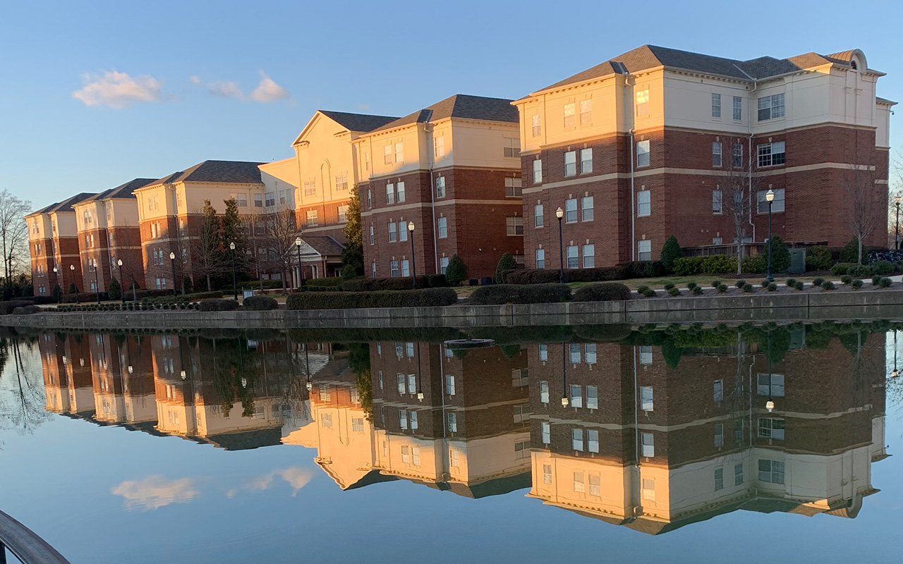 A tall building glowing with sunlight. In front of the building is a pond which almost perfectly reflects its image.